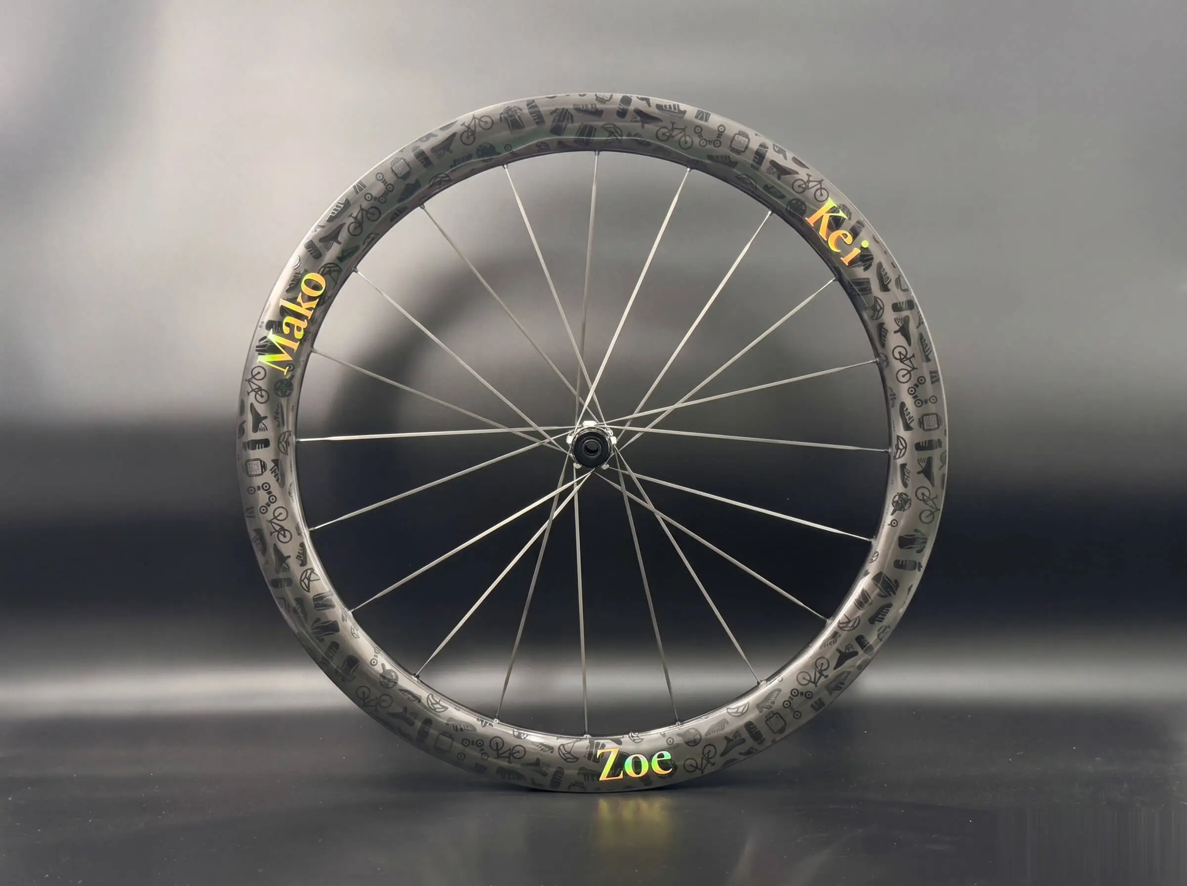 Custom OEM carbon wheel with rider-name decals (Mako, Kei, Zoe) and all-over cycling icon graphics, built by Light Travel Cycling