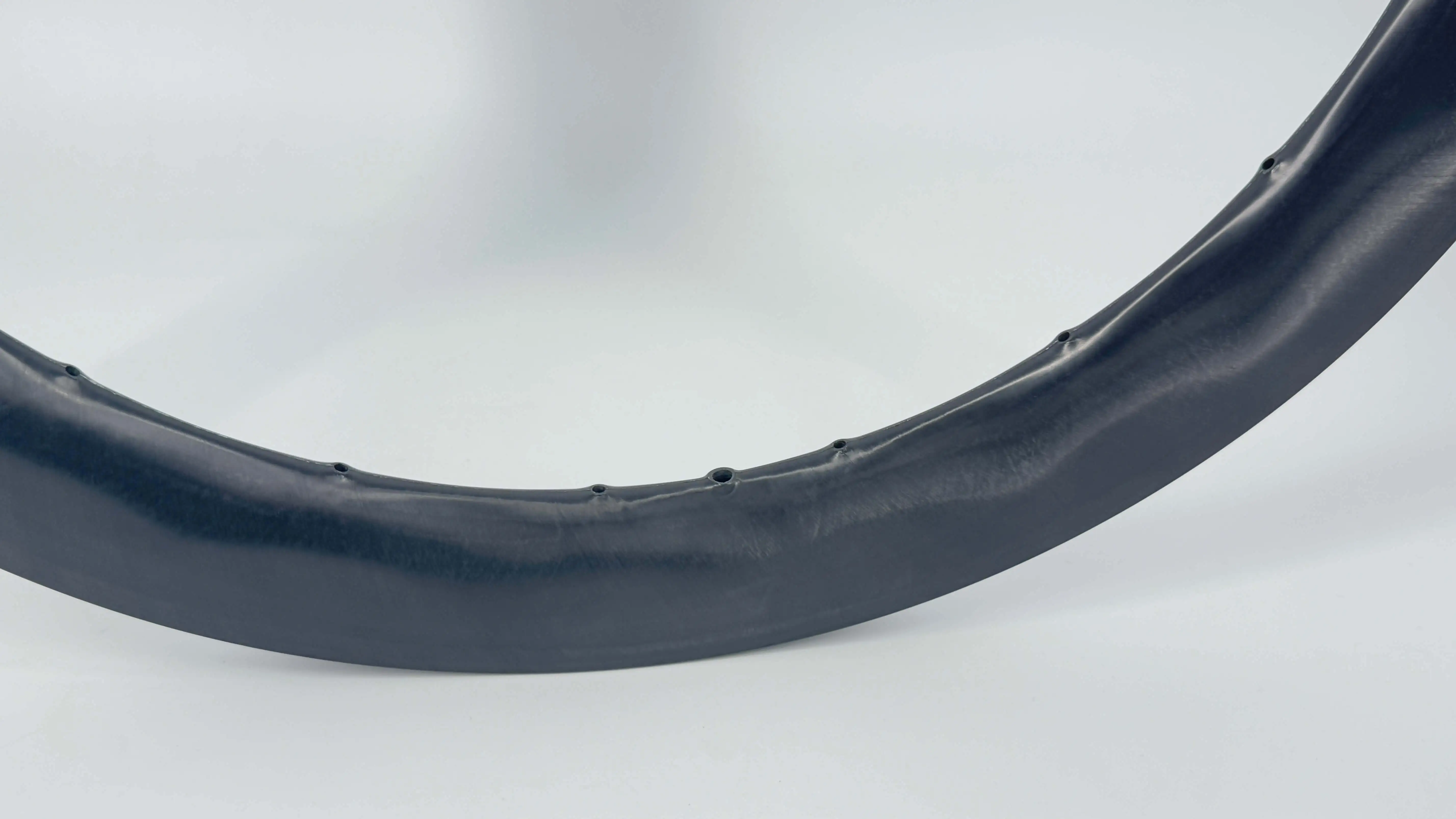 Close-up of a carbon rim spoke bed developed by Light Travel Cycling: precisely drilled spoke holes and valve hole on a glossy black rim