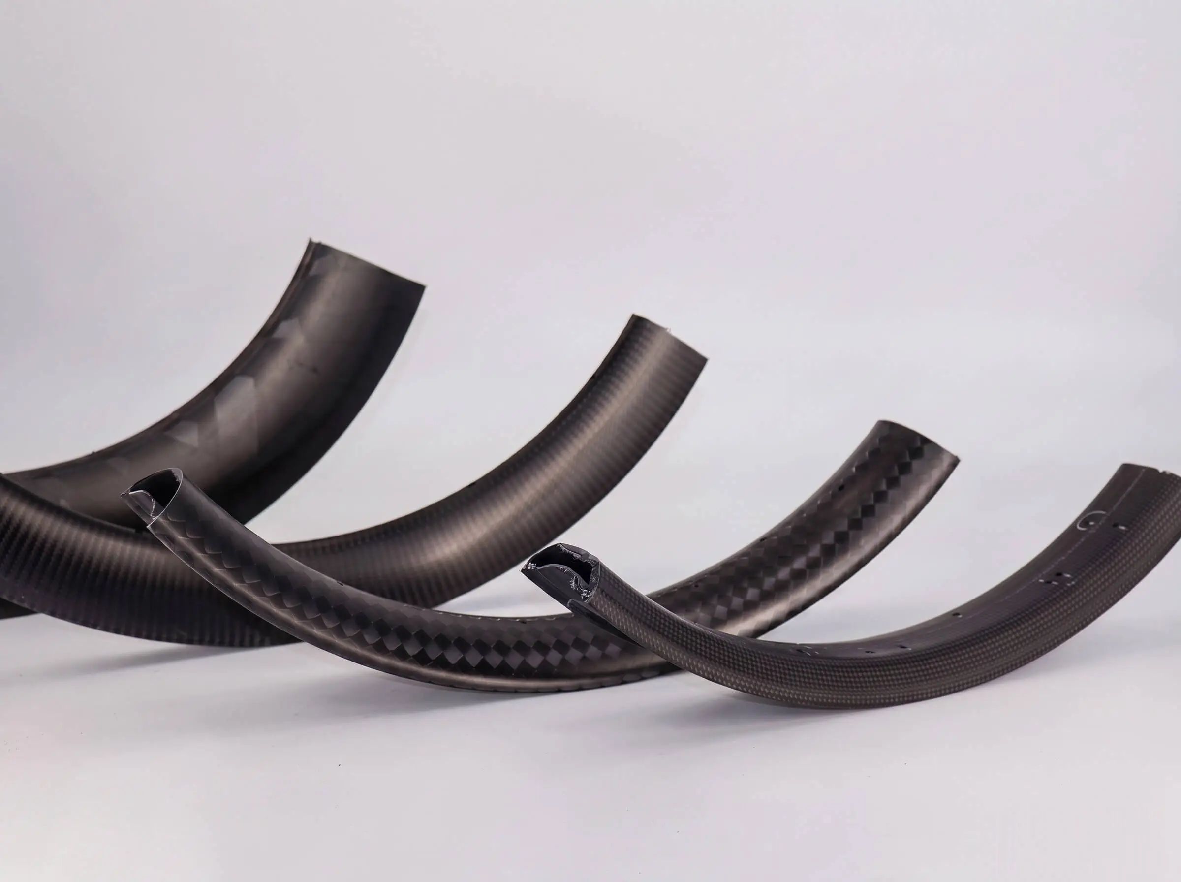 OEM carbon rim sections in different weaves and profile depths arranged side by side, cut ends showing the hollow cross-section structure, developed by Light Travel Cycling